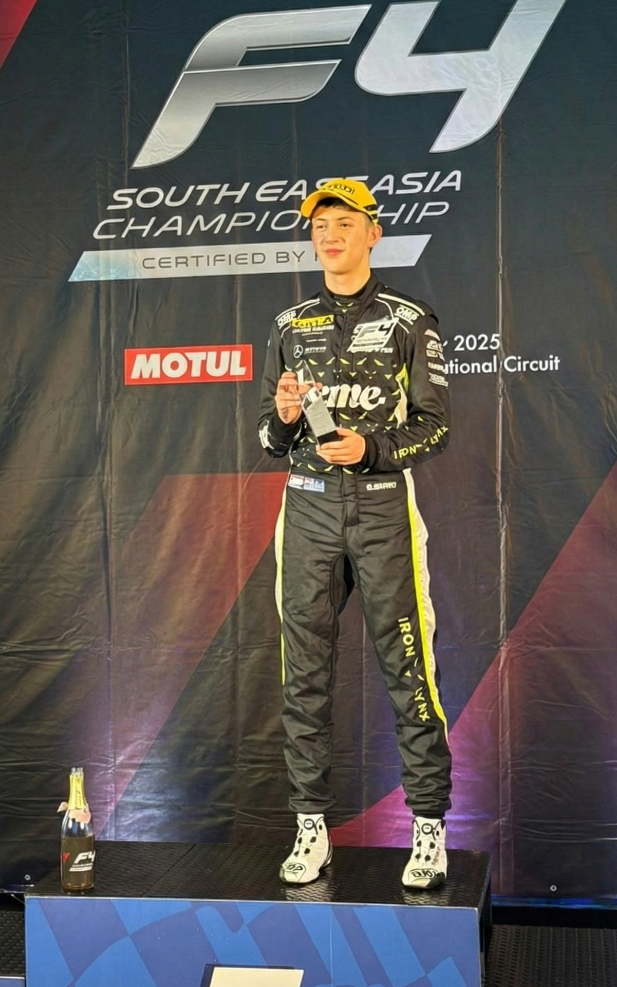 Josh Berry in racing suit holding a trophy on a podium with championship banner in the background