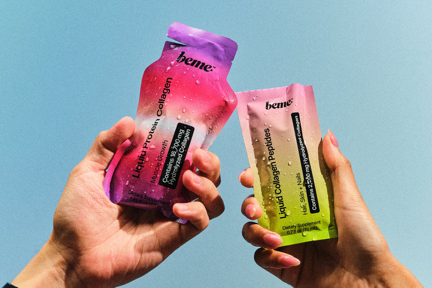 Two hands holding beme sachets against a blue sky.